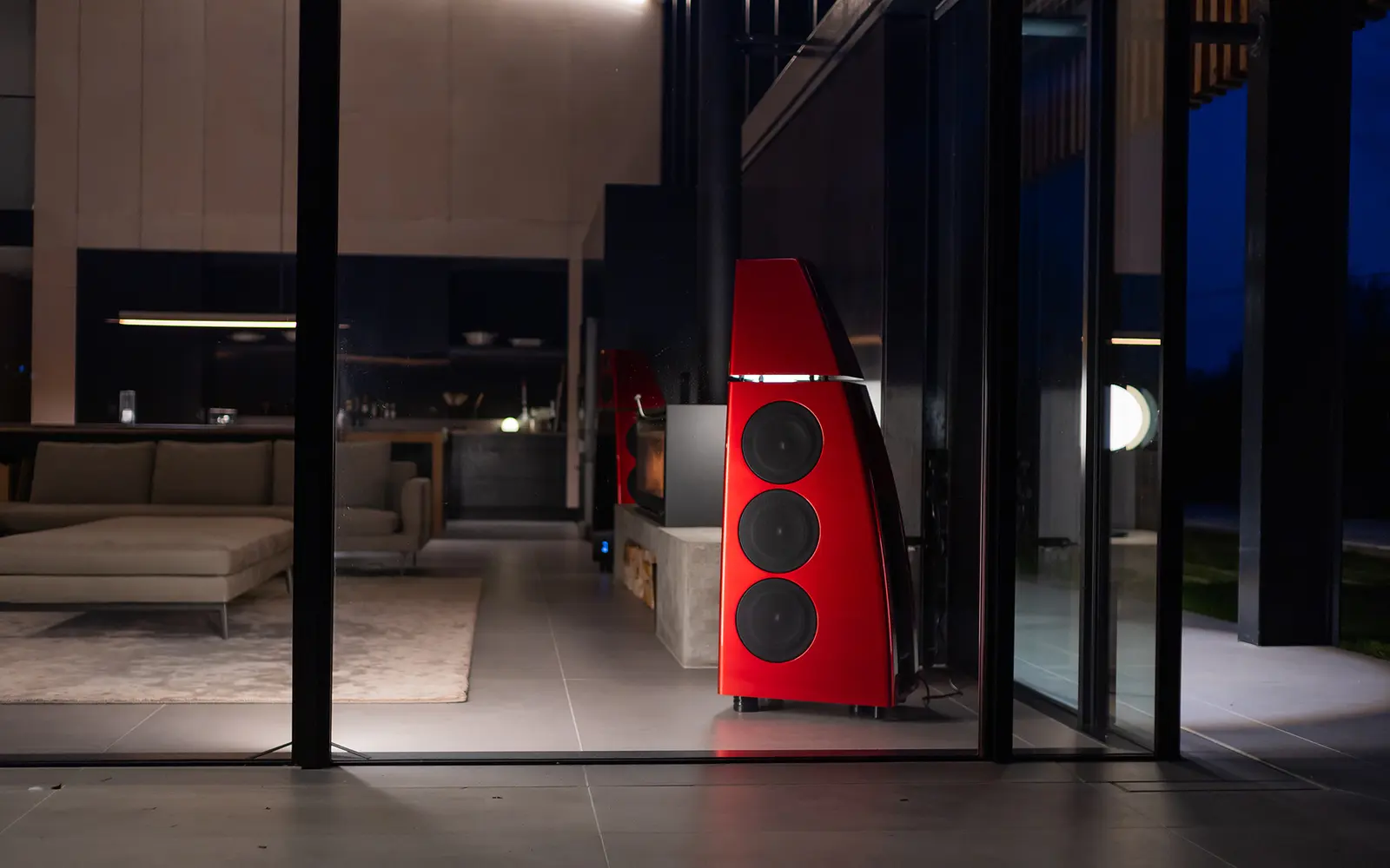 A Meridian DSP loudspeaker in a glass-walled modern home at dusk