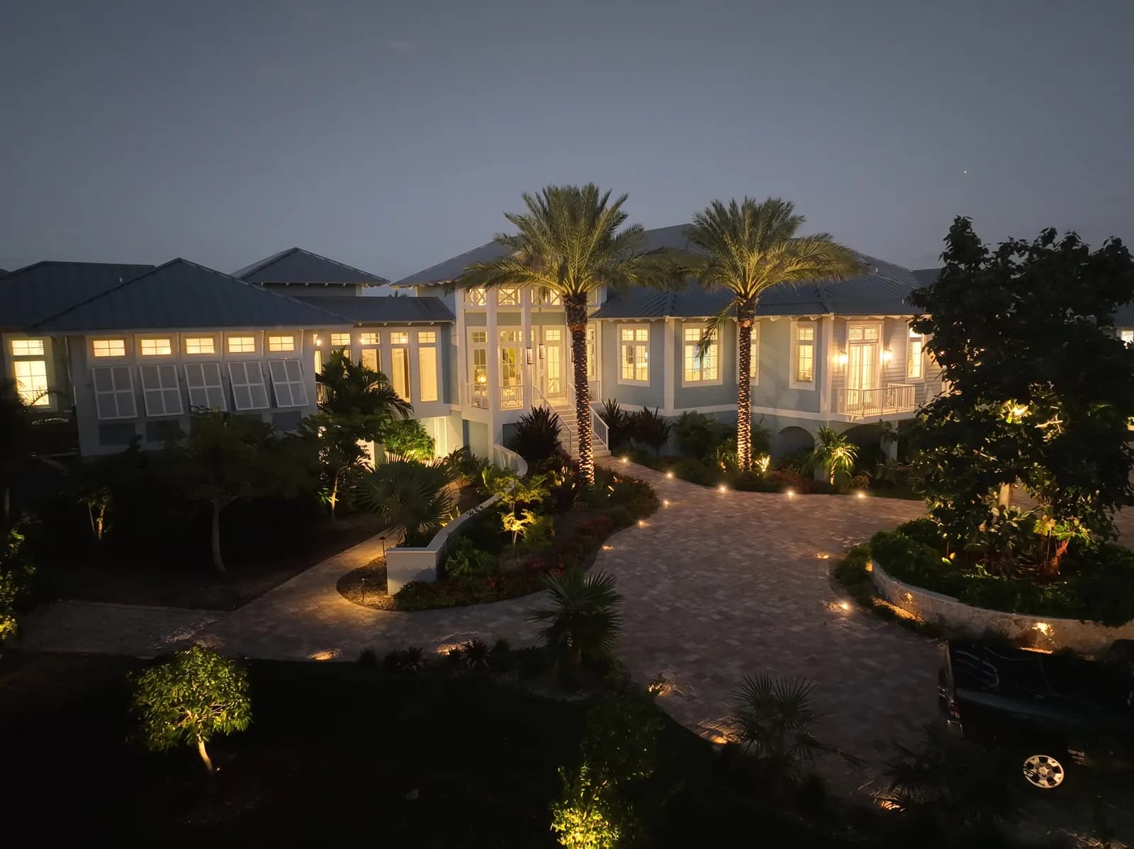 A coastal estate at dusk, drive and gardens lit in warm light