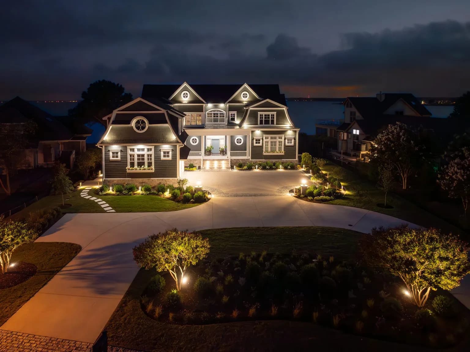 A shingled waterfront home floodlit against a night sky