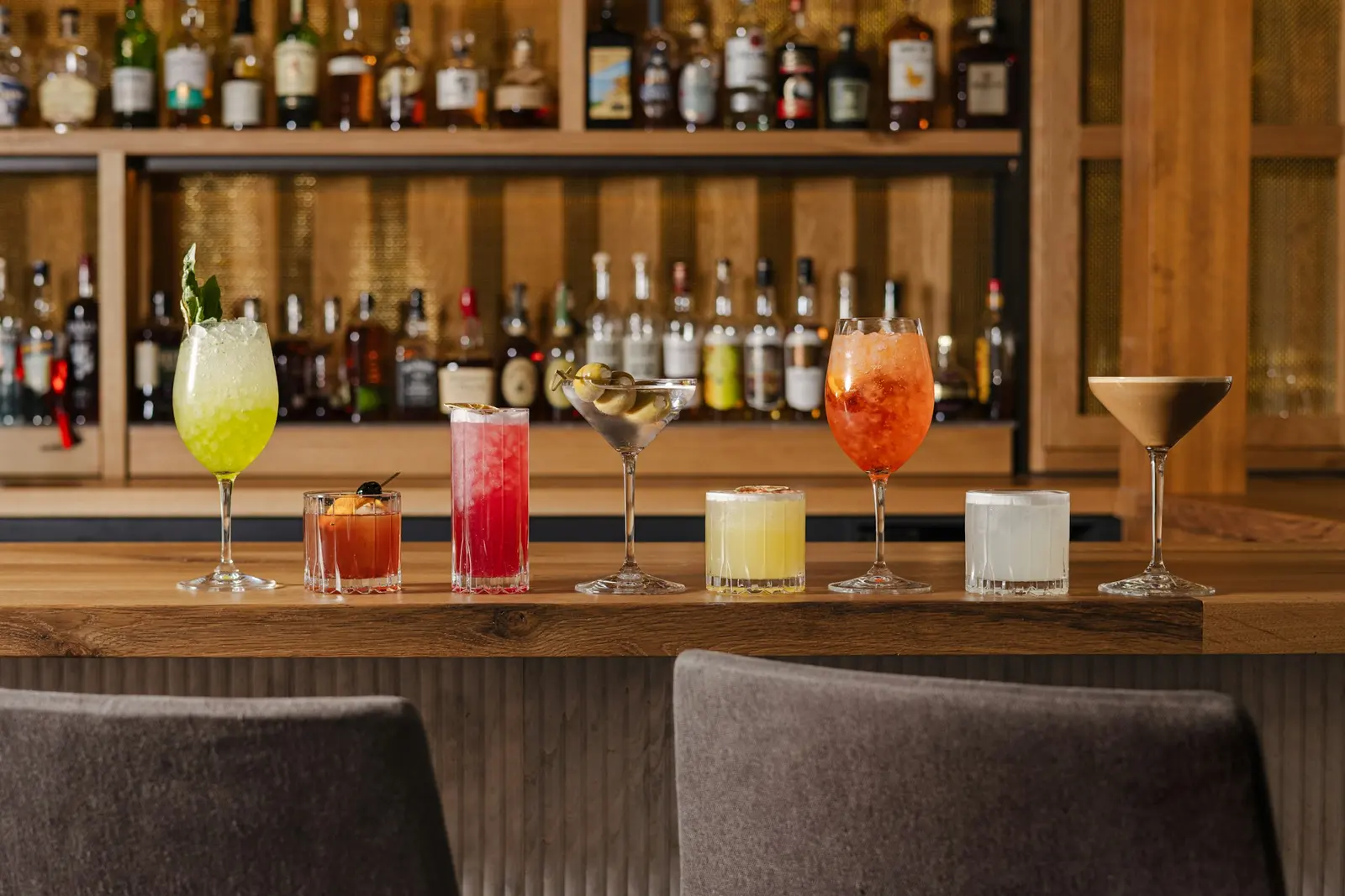 Elm's bar at night, a backlit bottle display glowing behind a row of cocktails