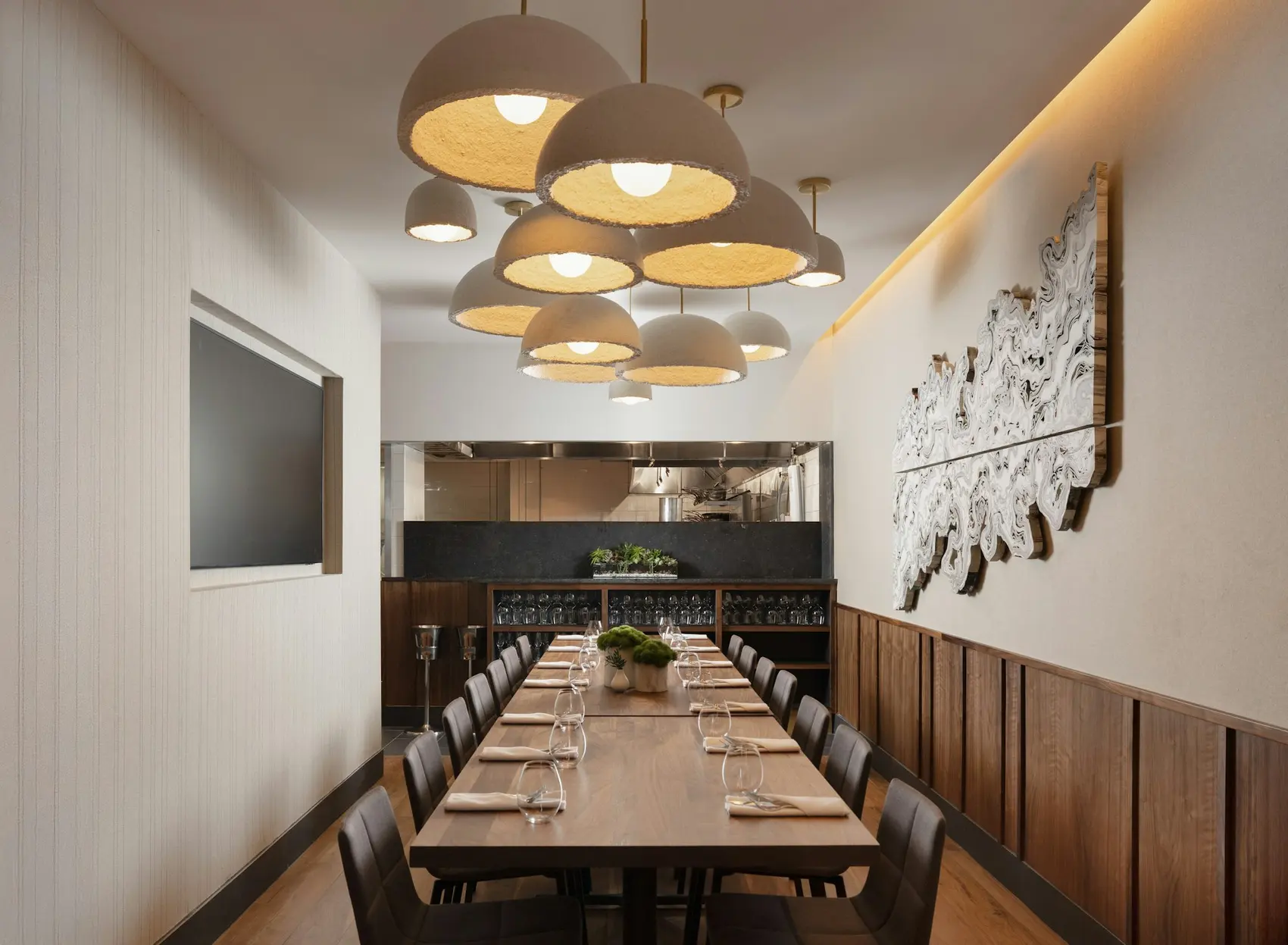 Elm's back private dining room, a cluster of dome pendants lit over a long table, a wall display beyond
