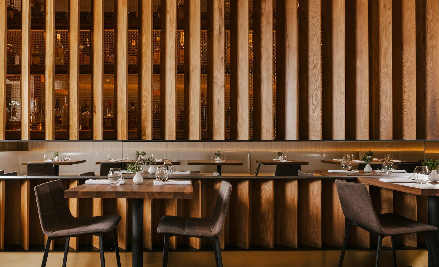 Elm's slatted walnut feature wall, concealed lighting glowing behind it, dining tables below