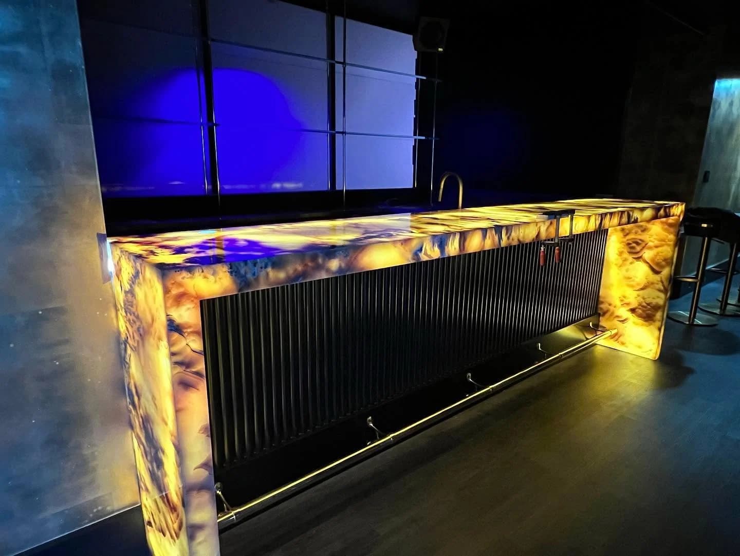 The backlit Pineapple Onyx bar glowing amber, the blue video wall beyond