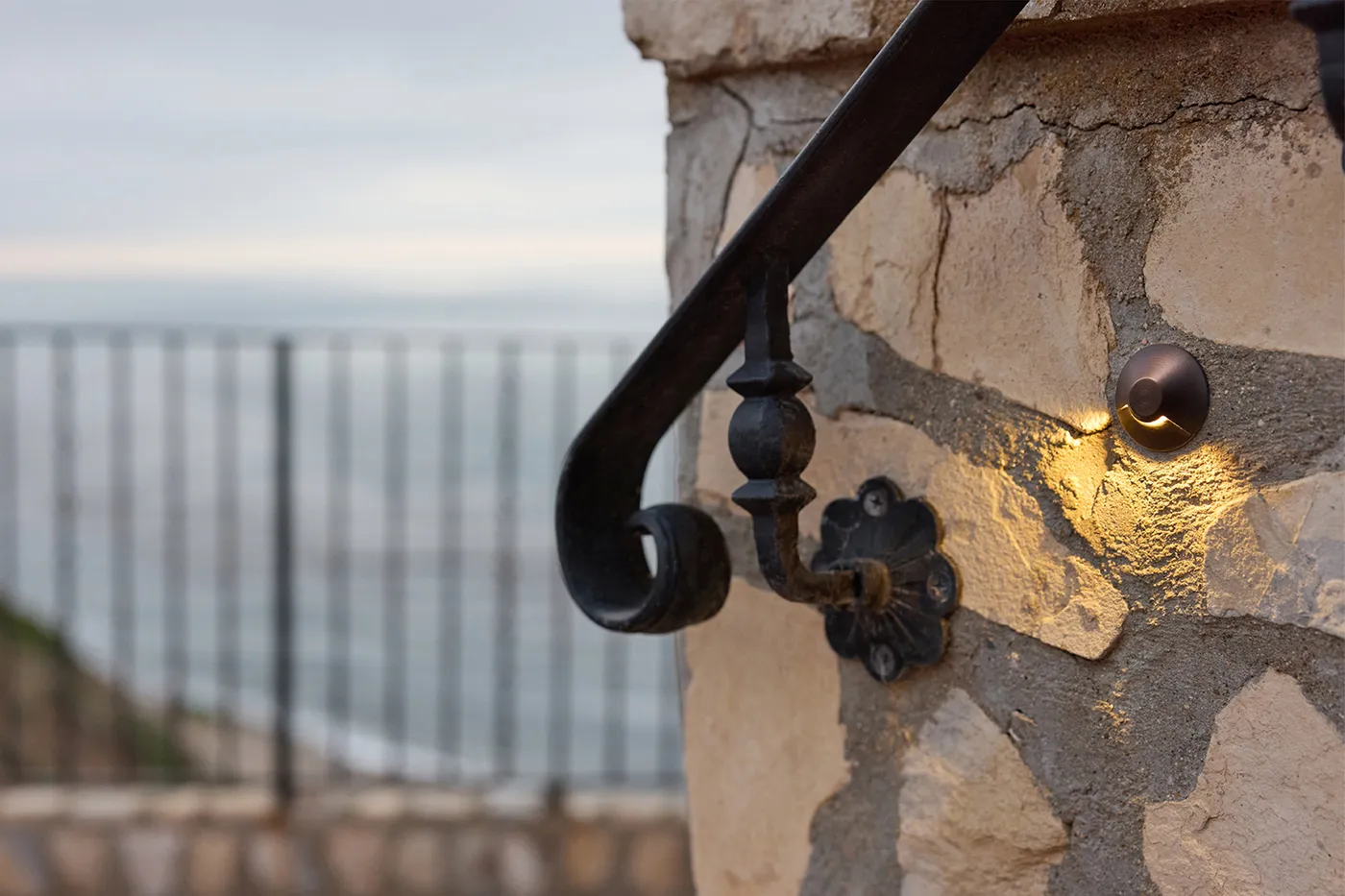 A hardscape light set into a stone pier, glowing low over a terrace at dusk